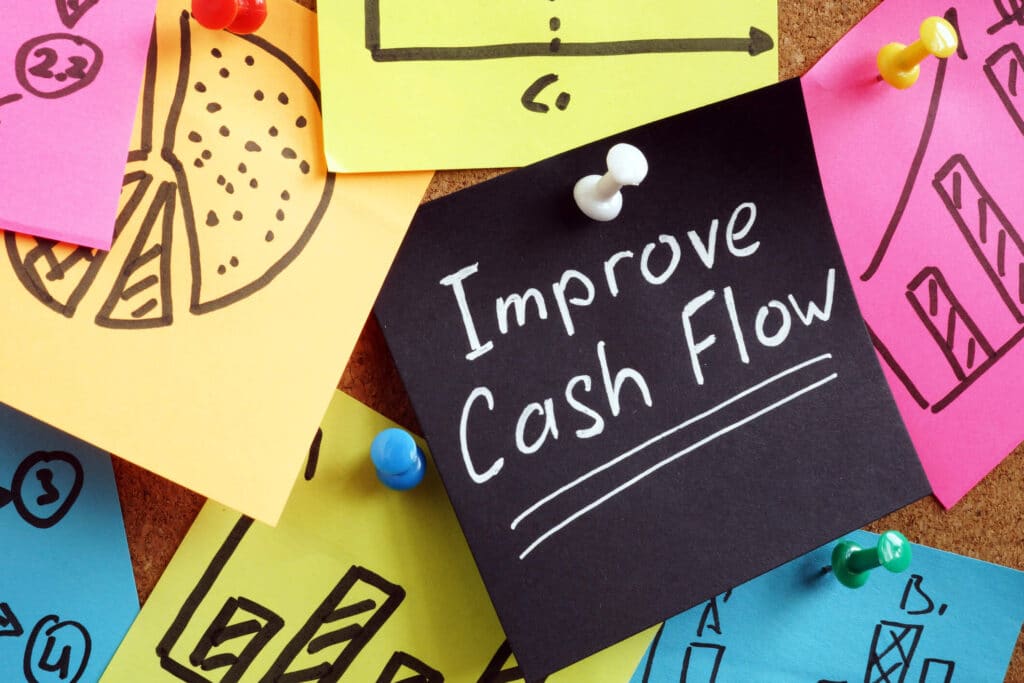 A sticky note with "Improve Cash Flow" attached to a board with other colorful notes. 