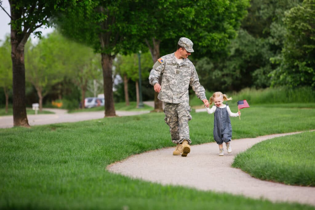 A soldier walking with his daughter in a nice neighborhood park. 